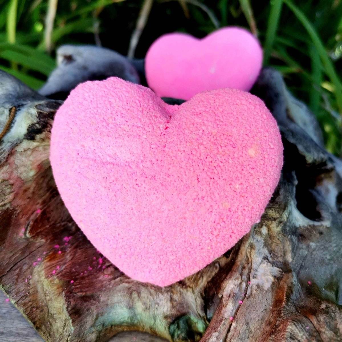 Pink heart-shaped bath bomb on driftwood, ideal for a luxurious and soothing experience.