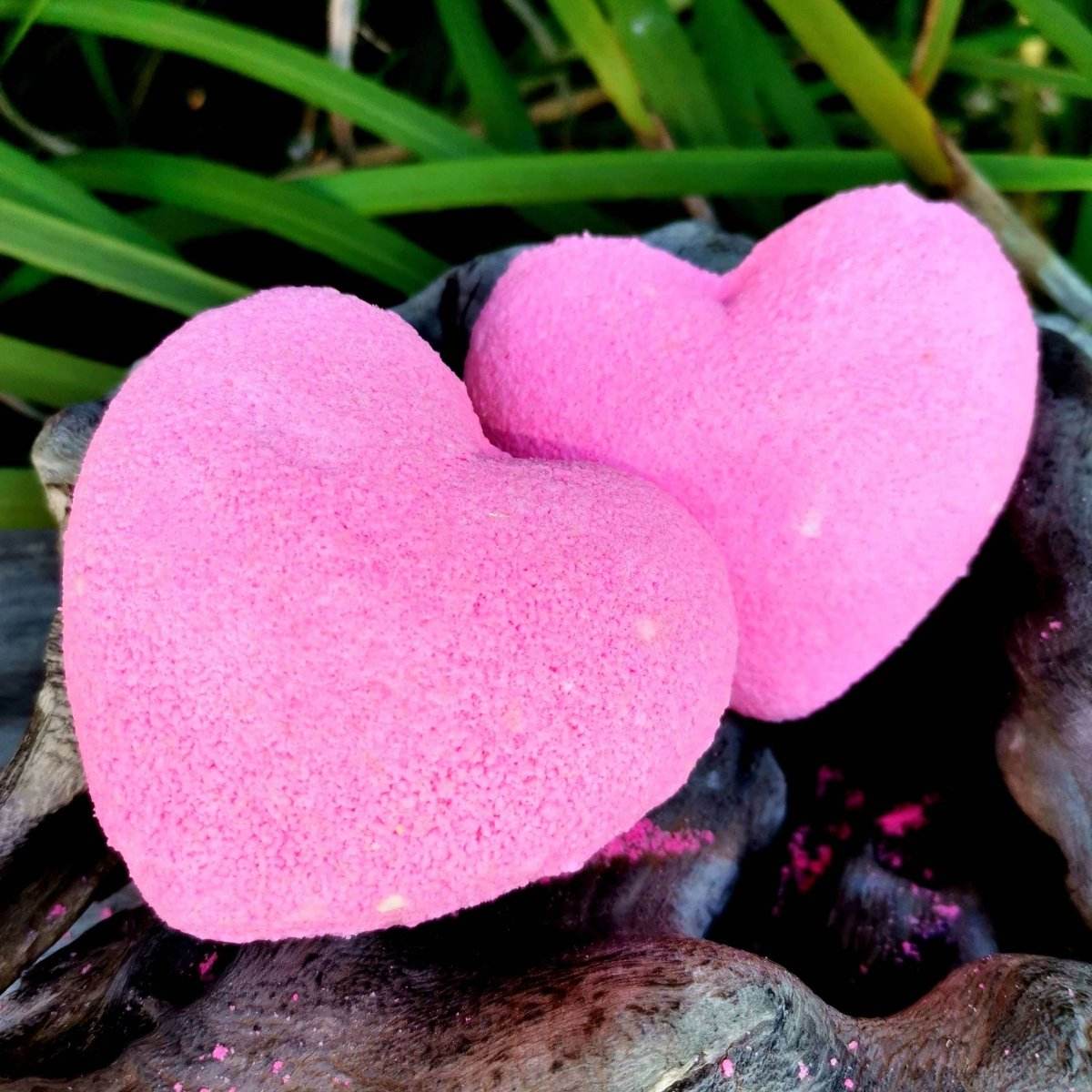 Heart-shaped pink bath bomb with nourishing hemp oil and shea butter on a wooden surface, ideal for luxurious baths.