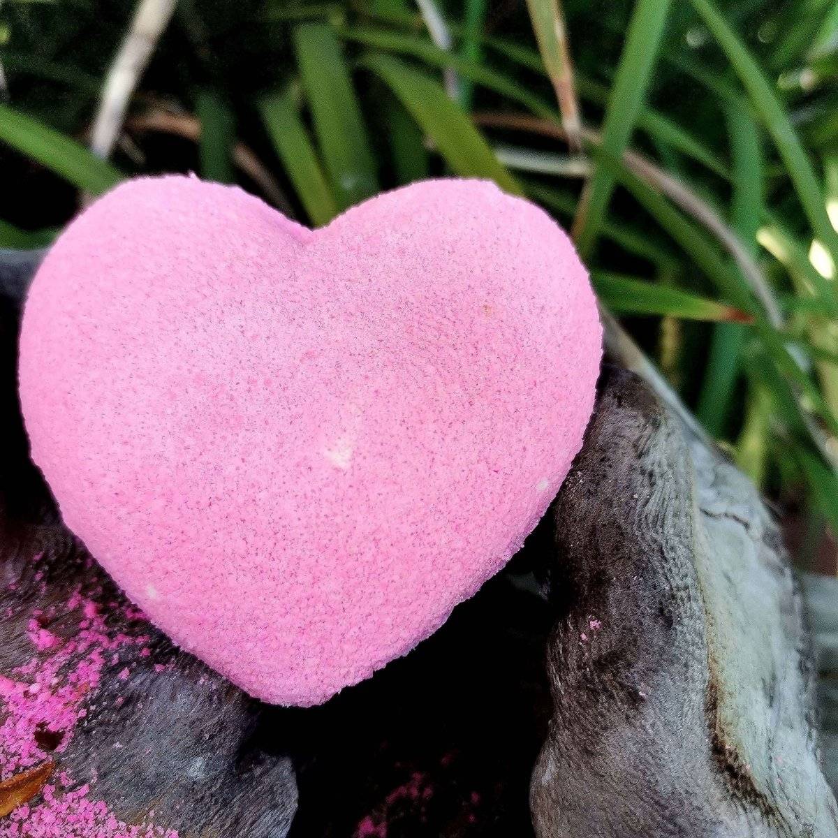 Heart-shaped pink bath bomb with nourishing hemp oil and shea butter, featuring a calming rose geranium scent.