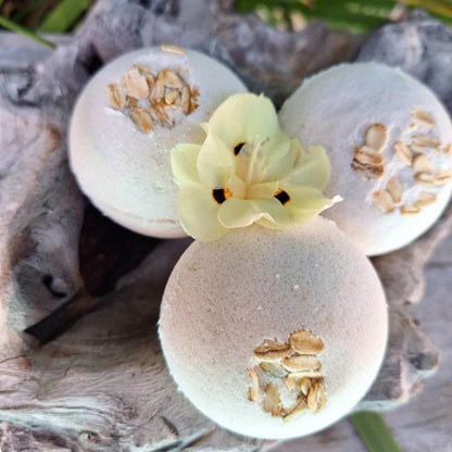 Three unscented bath bombs for sensitive skin with oatmeal and flower accents displayed on driftwood.