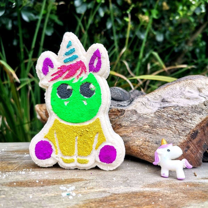 Unicorn-themed bath bomb by JUSTBLiSS on a wooden surface, colorful design, outdoor background.