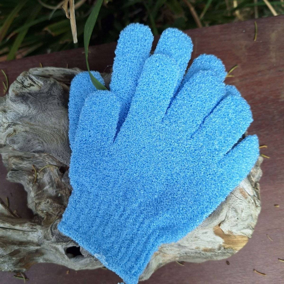 Blue exfoliating body scrub gloves on wooden surface.