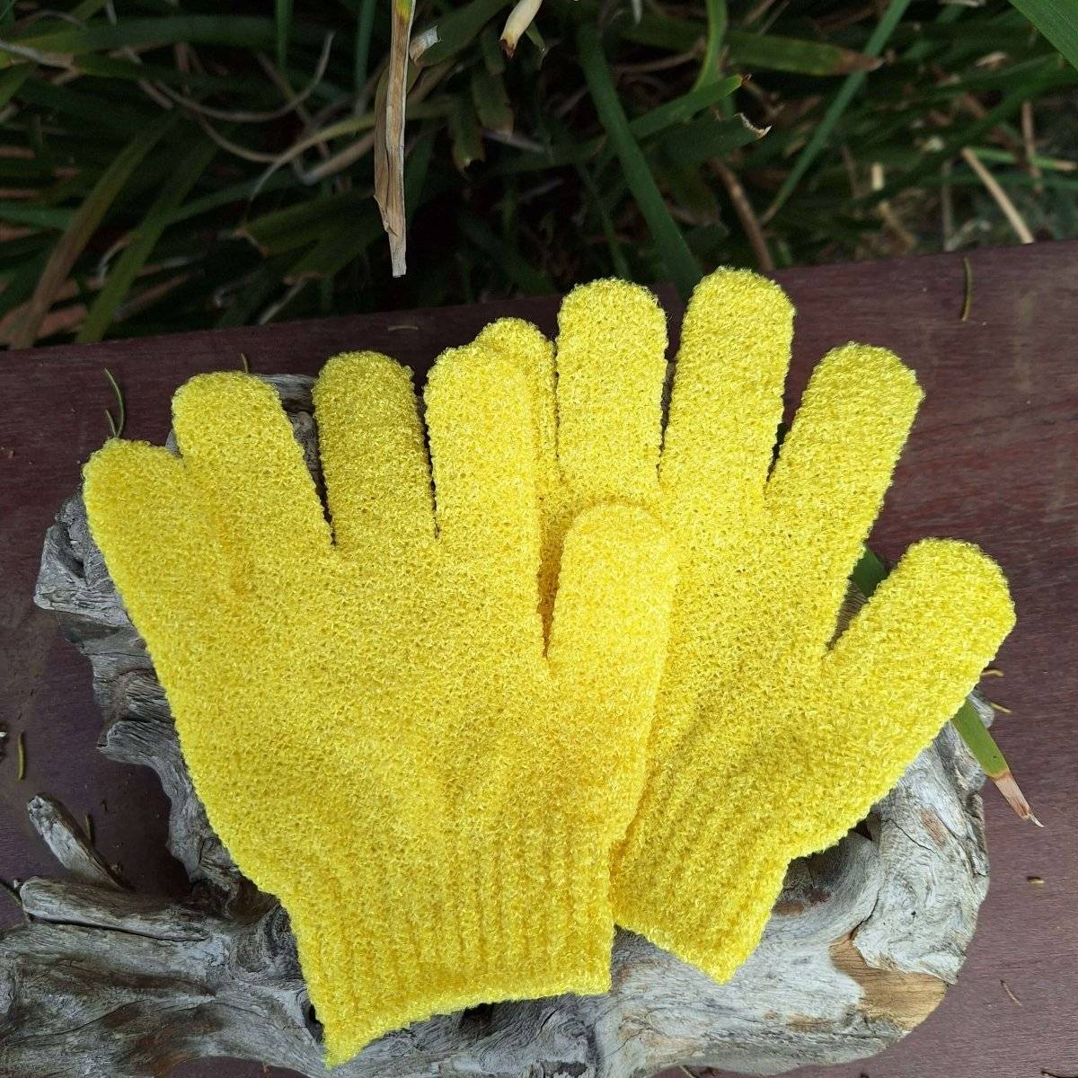 Yellow body scrub gloves on a wooden surface, ideal for exfoliating and enhancing skincare routine.