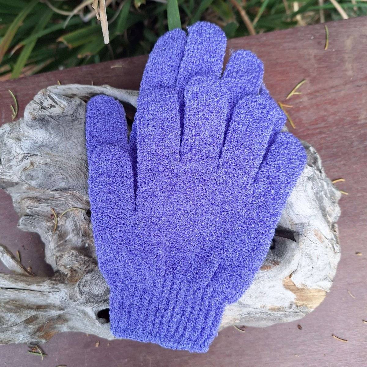 Purple body scrub gloves on a wooden surface for exfoliating and skincare.