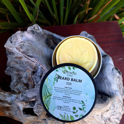 BEARD BALM Oud with lid off, revealing yellow balm, placed on textured surface.