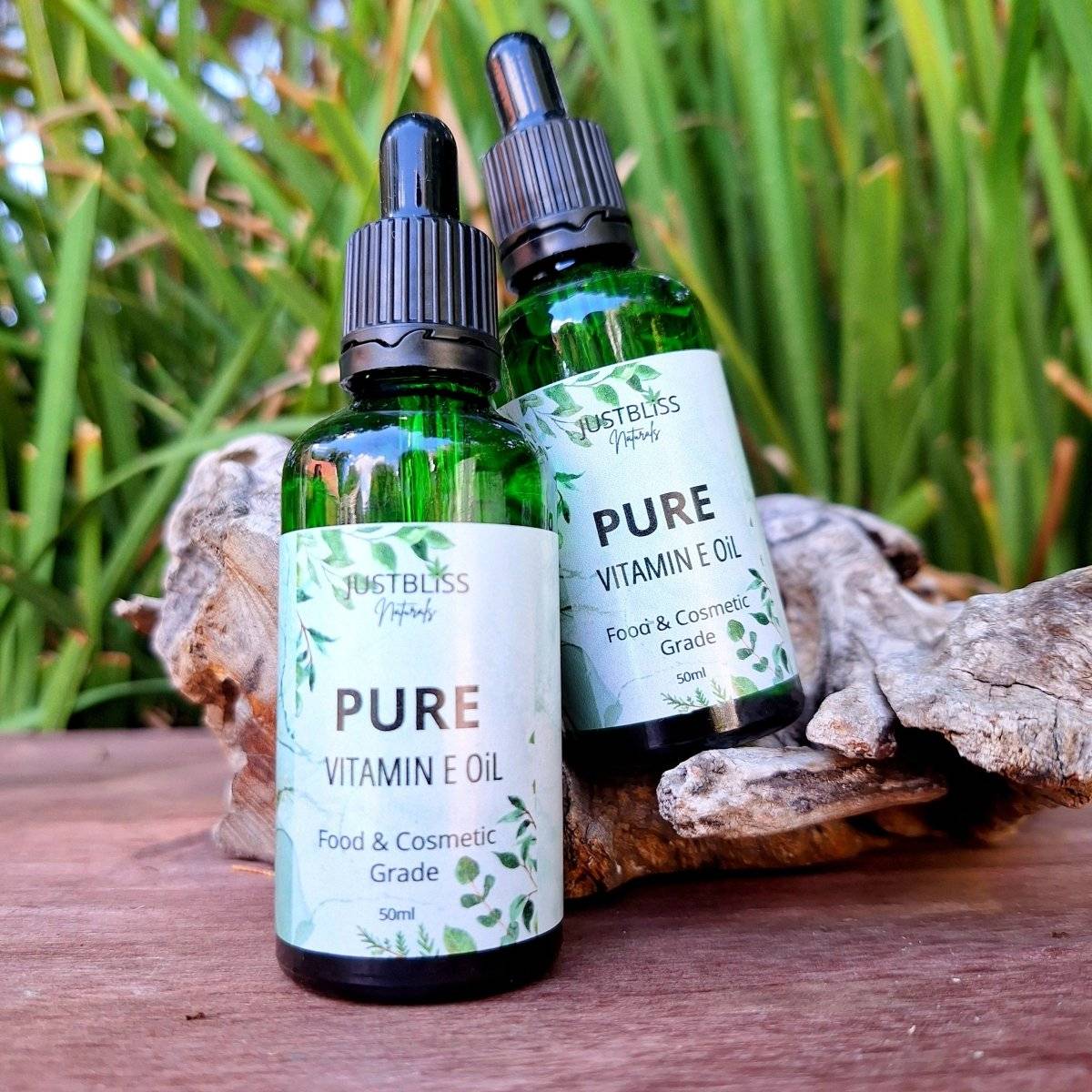 CARRIER OIL: Pure Vitamin E Oil bottles on a wooden surface with greenery in the background.