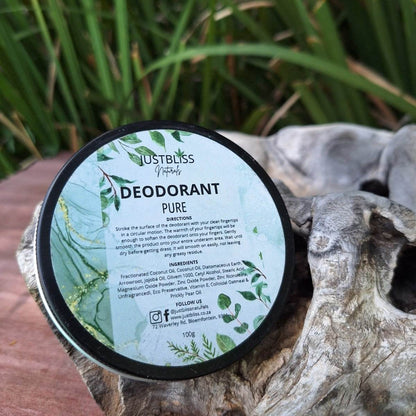 Natural deodorant tin with green foliage design in a natural outdoor setting.