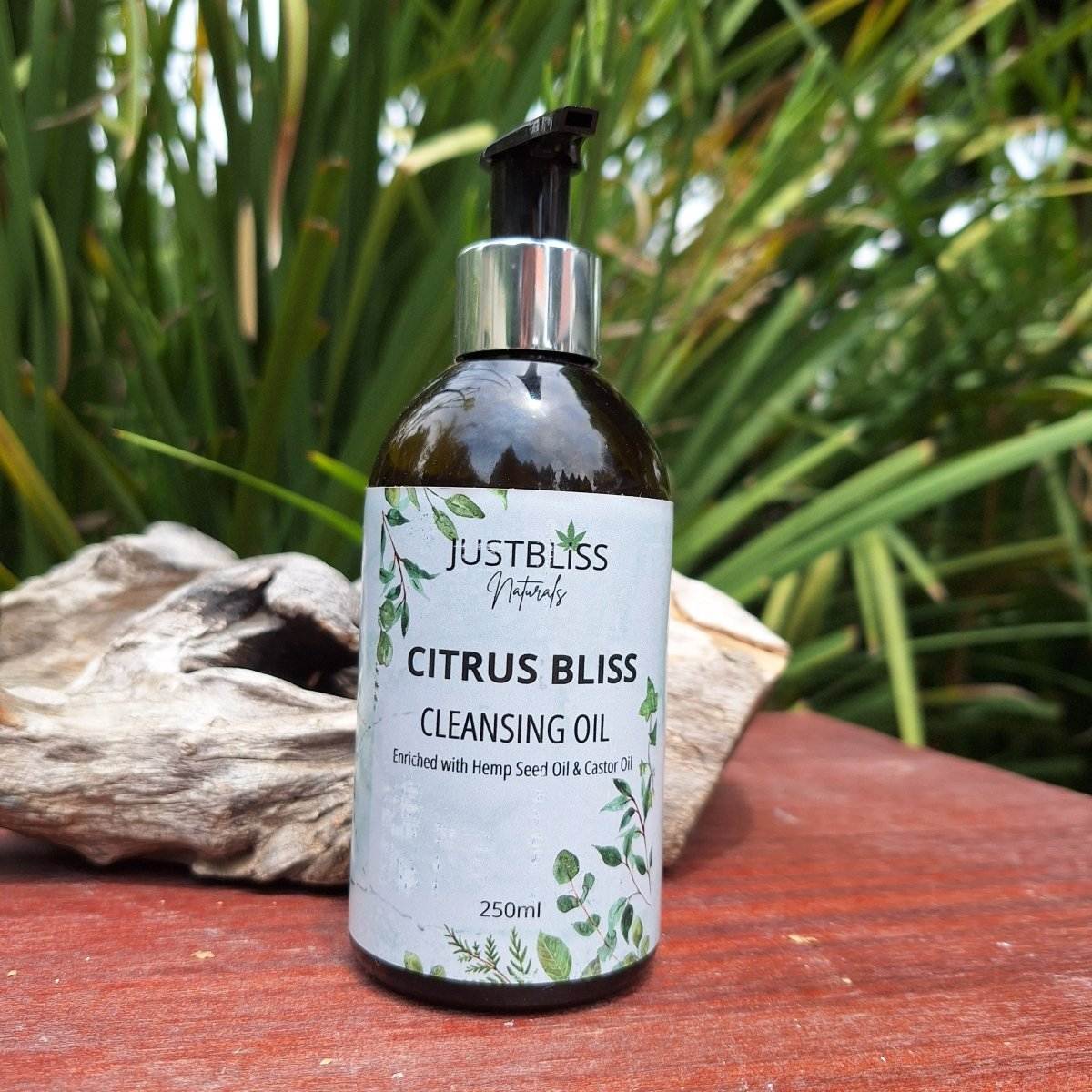 Citrus Bliss Facial Cleanser Oil bottle with hemp seed and castor oil, suitable for all skin types, on a wooden surface with greenery background.