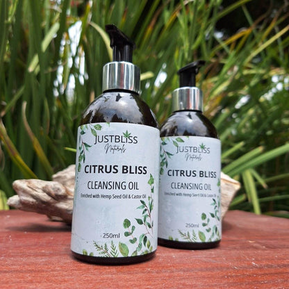 Citrus Bliss Facial Cleanser Oil bottles on wood table with greenery in background.