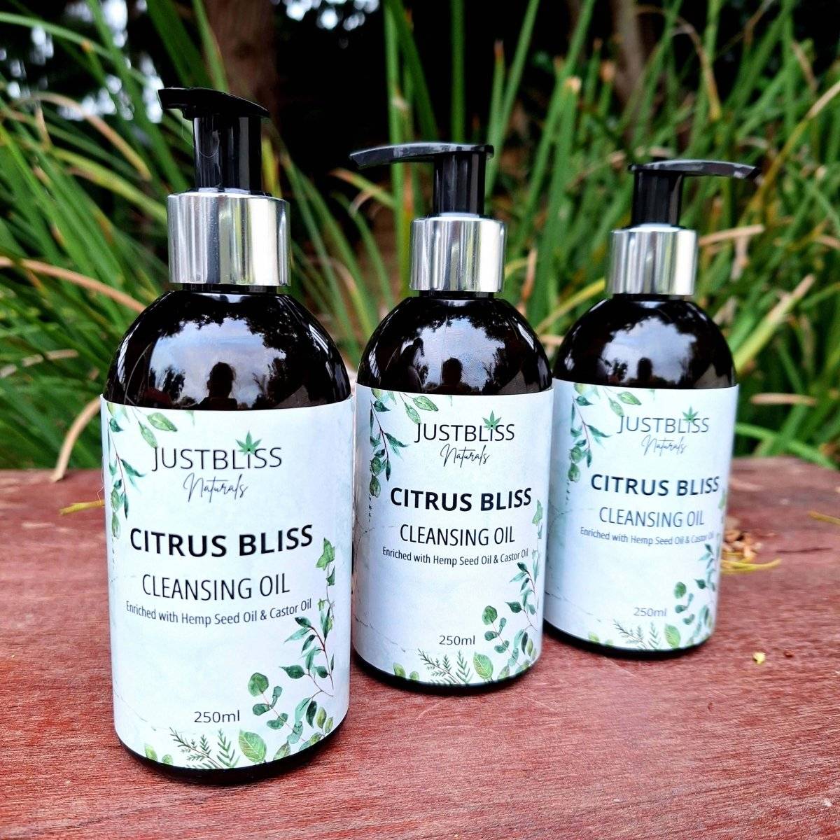 Citrus Bliss Facial Cleanser Oil bottles displayed outdoors on a wooden surface.