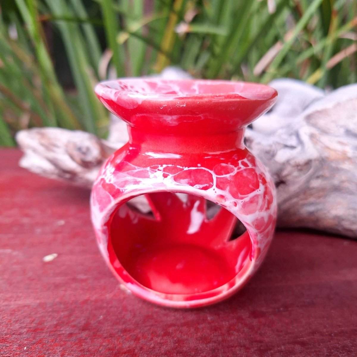 Red essential oil burner from Blissful Home Aromatherapy Gift Box 1, set on a wooden surface with greenery background.