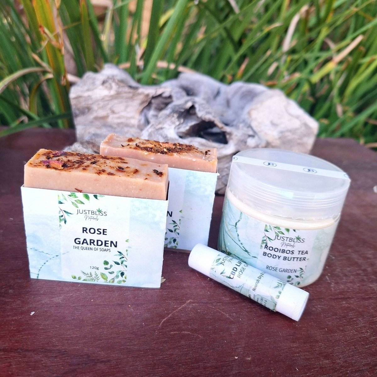 Bath, Body & Lip Set Aromatic Geranium with soap bars, rooibos tea body butter, and geranium lip balm displayed outdoors.