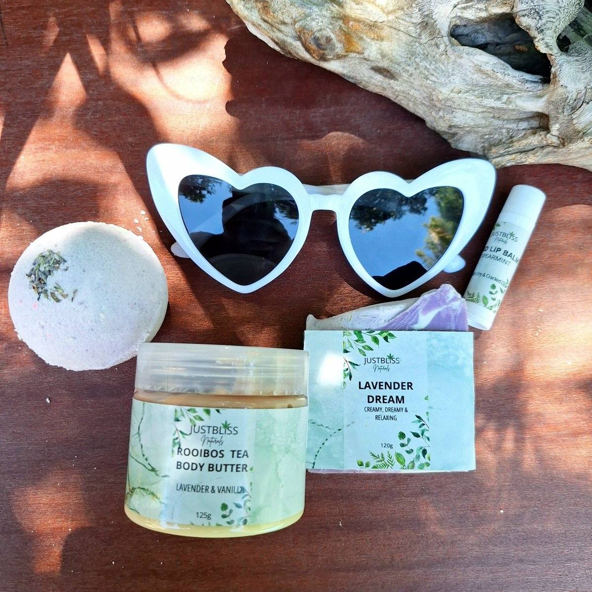 Bride-to-Be Gift Box with lip balm, Rooibos Tea body butter, Lavender Dreams soap, lavender bath bomb, and heart-shaped sunglasses on wooden background.