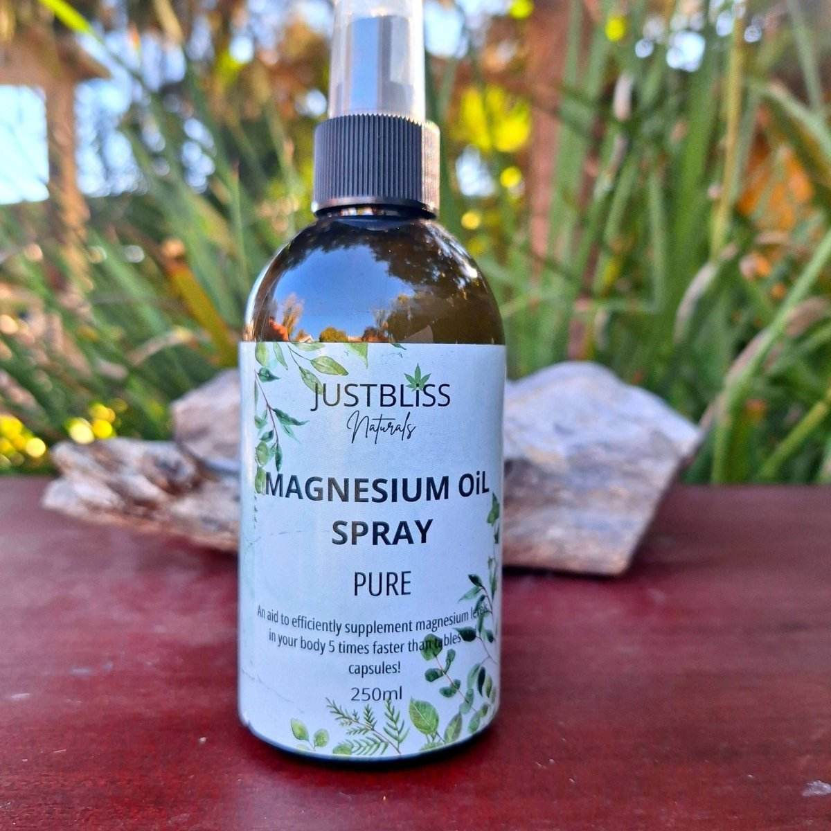 Pure Magnesium Oil Spray bottle on wooden table with greenery background.