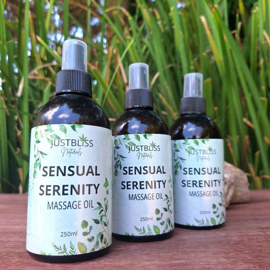 Sensual Serenity Massage Oil bottles with green labels on a wooden surface, surrounded by lush greenery.