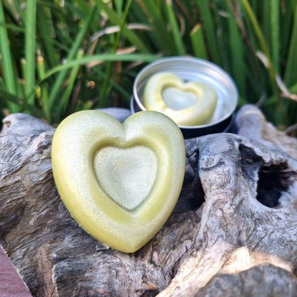 Heart-shaped lotion bar with nourishing oils, ideal for dry skin, displayed on a rustic surface with an open reusable tin.