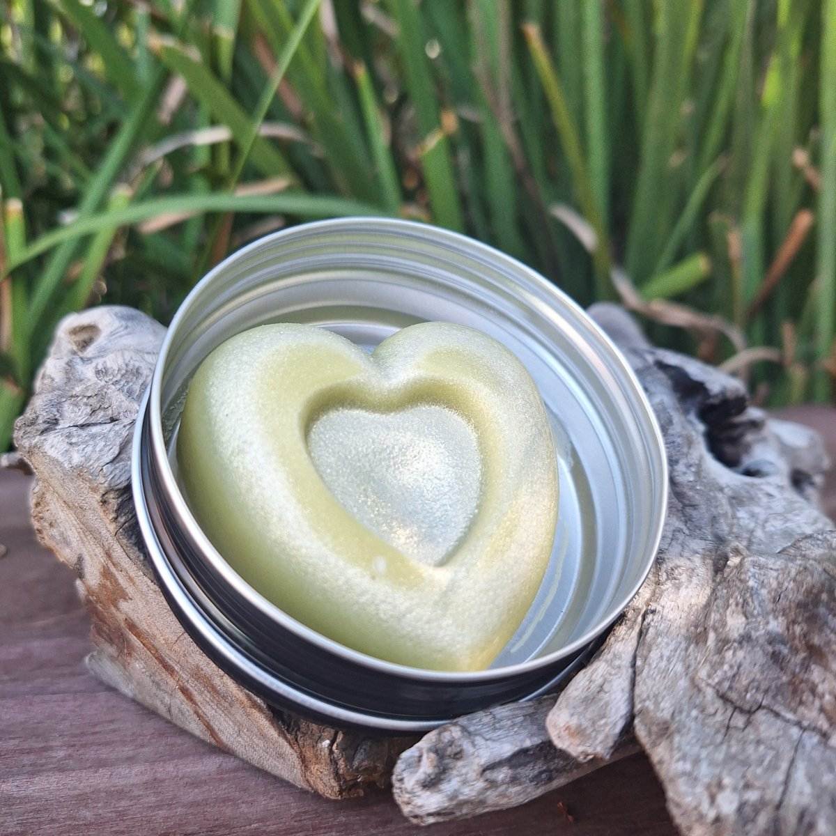 Heart-shaped lotion bar in reusable tin on natural wooden surface.