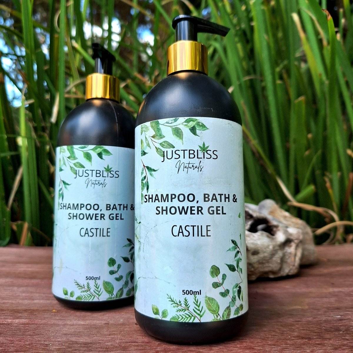 3-in-1 SHAMPOO, BATH & SHOWER GEL bottles with gold pumps on wooden surface, lush green background